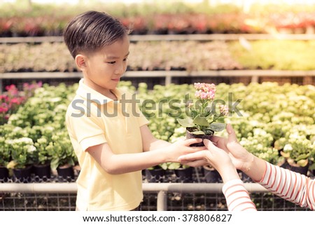 Vintage color, Young Asian boy give a little plant in small pot to the woman hand in the garden shop with yellow sunlight from the corner of the picture. Concept Earth day