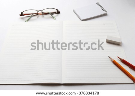 Blank notebook with pencil, red pencil, notepad, glasses, and eraser on white background.