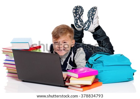 Happy schoolboy lying on floor with laptop, backpack and books isolated on white background