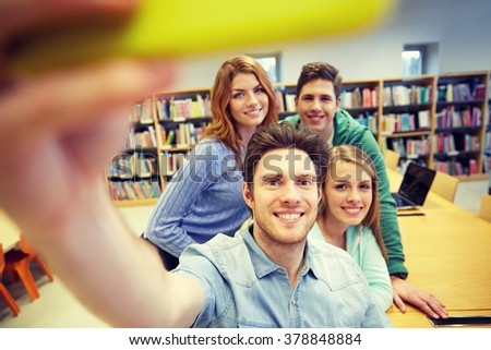 people, technology, education and school concept - happy students or friends with smartphone taking selfie in library
