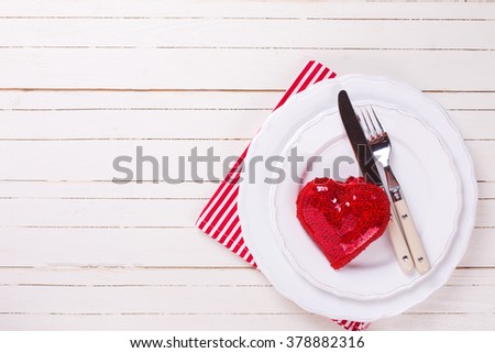 Romantic table setting. Red and  white. Decorative red heart, knife and fork on white plate on white  wooden background. Selective focus. Selective focus. Place for text.
