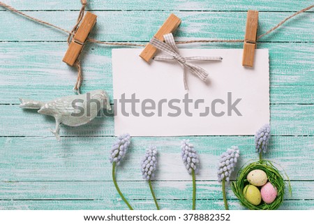 Easter background. Fresh blue flowers, Easter eggs in nest,  decorative bird  and empty tag on clothes line on turquoise   wooden background. Selective focus. Place for text. 
