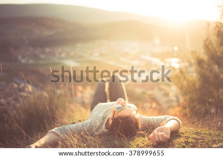 Carefree happy woman lying on green grass meadow on top of mountain edge cliff enjoying sun on her face.Enjoying nature sunset.Freedom.Enjoyment.Relaxing in mountains at sunrise.Sunshine.Daydreaming Royalty-Free Stock Photo #378999655