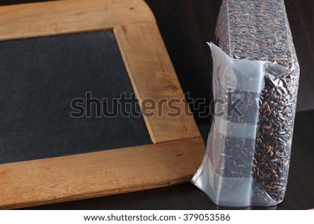 The slate board and rice berry put on dark color wooden background represent the raw food material concept related idea.