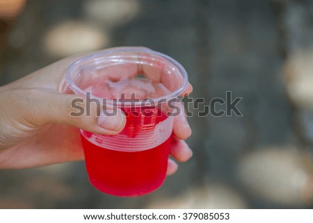 Female hand holding water glass with red liquid drink background
