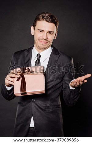 Portrait young businessman in black suit looking at camera with gift box. Christmas, x-mas, winter, valentine's day, birthday, happiness concept. Image on a black background.