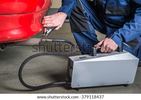 A diagnostic sensor is applied to the ehaust of a car by a mechanic, measuring the composition and substances in the exhaust fumes Royalty-Free Stock Photo #379118437