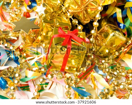 Small golden gift with red ribbon around colored confetti and christmas decoration. Shallow DOF.