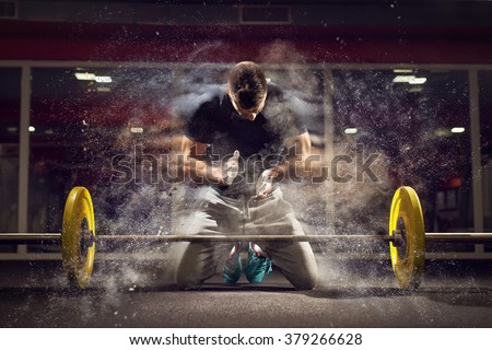 Handsome weightlifter preparing for training. Shallow depth of field, selective focus on hands and dust. Royalty-Free Stock Photo #379266628