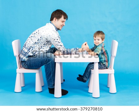 Funny father and little son competing in arm wrestling on blue background