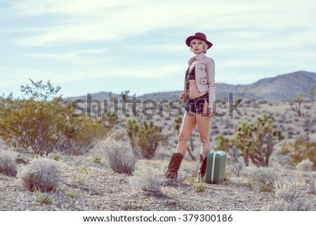 fashionable woman traveler walking with suitcase and luggage in desert
