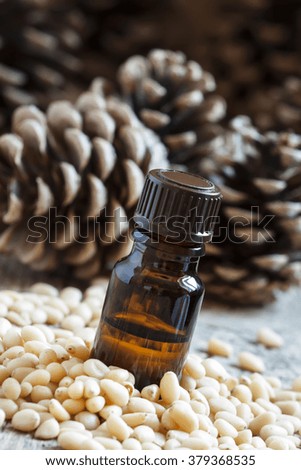 Essential oil of cedar in a small brown bottle, pine nuts, pine cones on old wooden background, selective focus