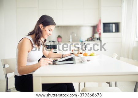 Young brunette is reading the newspaper while having breakfast at home.Modern woman lifestyle-healthy fitness breakfast,coffee and fruit,reading motivational quotes.Starting your day,positive energy Royalty-Free Stock Photo #379368673