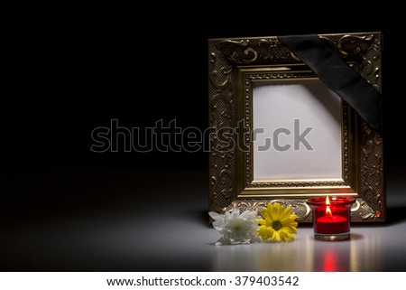 blank golden mourning frame with flowers and candle on dark background