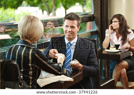 Young businessman and businesswoman having a meeting in cafe, exchanging business cards.