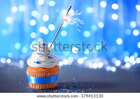 Cupcake with white cream icing and sparkler on a glitter background
