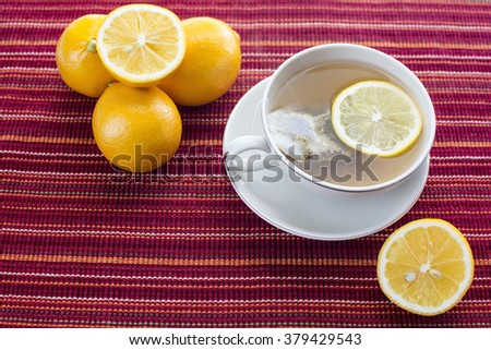 Lemon hot tea with tea bag in a cup and lemon fruits on red stripes platemat 