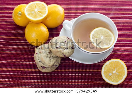 Lemon hot tea with white chocolate chip cranberry cookies and lemon fruits on red stripes platemat
