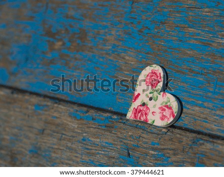 Beautiful delicate wooden button in shape of heart on old wooden background with a blue shabby paint, a background for post card, handmade. Buttons with a picture of roses, shabby chic background.
