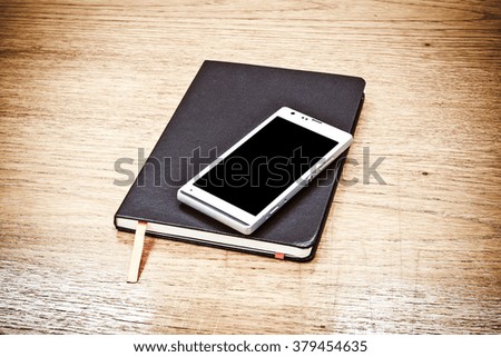 Black leather business diary and Mobile phone on wood table background, Vintage color filter.