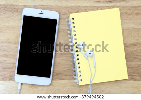 Phone and notebook with blank screen on wooden background.