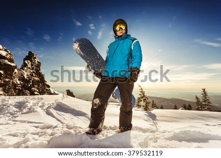 Snowboarder stands on mountain top and sunset backdrop. Sheregesh resort, Siberia, Russia