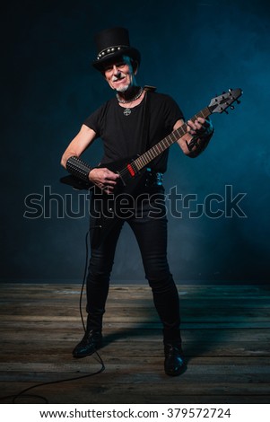 Heavy metal senior man with electric guitar in front of dark blue background.