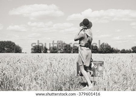Back view of beautiful young lady with suitcase on countryside landscape blue sky outdoors background. Vacation or immigration concept. Black and white photography