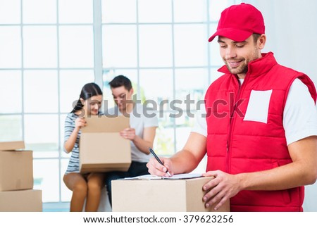 Delivery service worker in uniform delivering parcels to happy couple. Man with box signing document