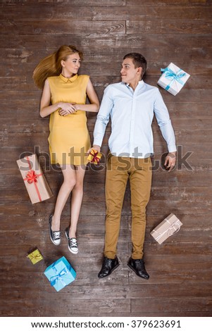 Top view creative photo of beautiful young couple on vintage brown wooden floor. Couple lying with gifts