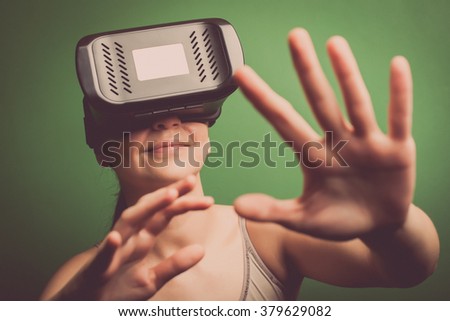 Color shot of a young woman looking through some VR glasses, a device with which one can experience virtual reality on a mobile phone.