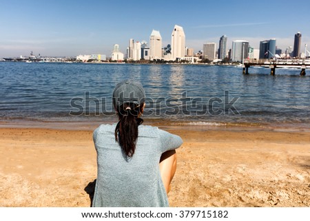 Back view of a woman sitting on beach and looking out into bay of San Diego, California. 