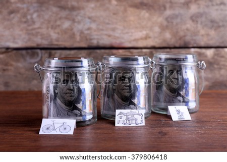 Rolls of dollar banknotes for different needs in glass jars on wooden table