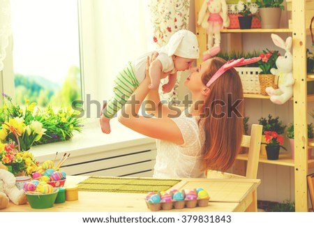 happy family celebrating easter mother and baby bunny ears at home with colorful eggs and flowers