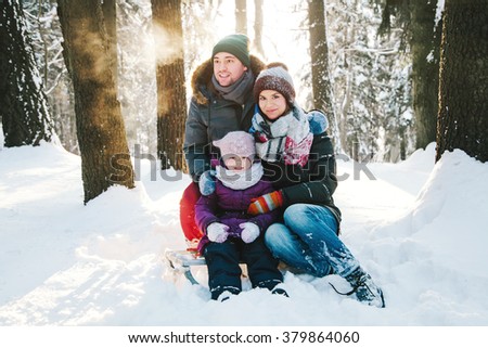 Portrait of a positive young family in the winter forest at sunset and smiling