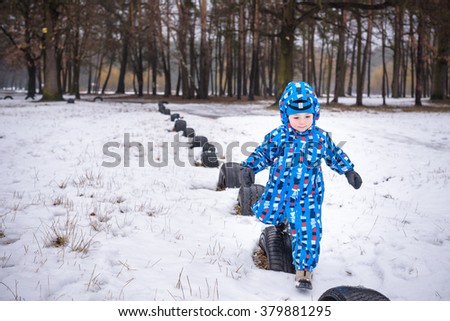 Winter portrait of kid boy in colorful warm clothes, playing alone outdoors. Active leisure with children in winter on cold snowy days. Happy child having fun with snow in forest or park