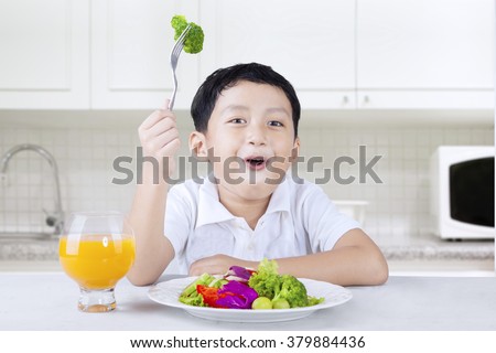 Picture of a little boy sitting in the kitchen and eats vegetable salad with orange juice