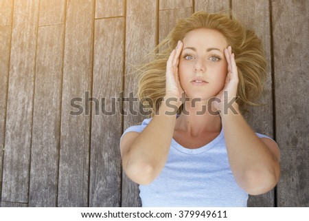 Closely image of a young charming model posing for advertising natural cosmetics while lying on a wooden background with copy space, attractive blonde woman with beautiful blue eyes looking at camera