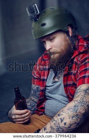 Bearded tattooed man in a red shirt posing with a longboard.