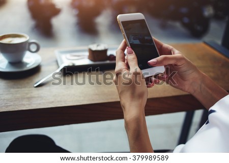 Close up of women's hands holding cell telephone with blank copy space scree for your advertising text message or promotional content, hipster girl watching video on mobile phone during coffee break  Royalty-Free Stock Photo #379989589