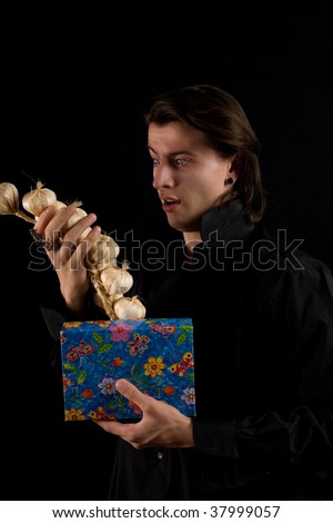 Funny shot of amazed vampire with gift box taking out garlic, isolated on black background