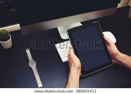 Closeup image of man's hands holding touch pad with blank copy space screen for your text message or content against business workplace with pc deskpot, wireless keyboard, computer mouse, hand watches