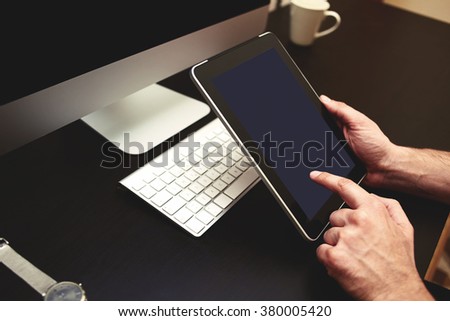 Cropped image of man's hands using portable digital tablet with blank copy space screen for your text message or promotional content against freelancer workplace with pc, wireless keyboard,cup of tea 