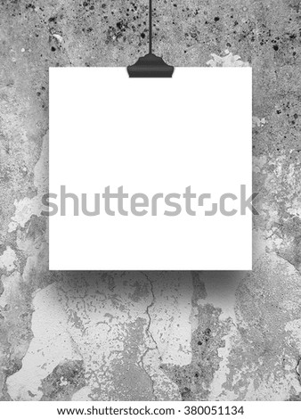 Close-up of one hanged square paper sheet frame with clip on grey scratched and weathered concrete wall background