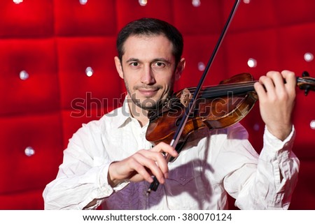 Young musician playing the violin in a restaurant on a red wall.