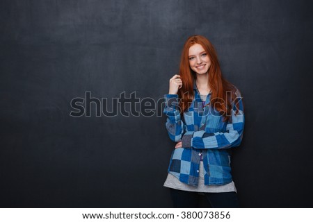 Happy beautiful young woman with long red hair standing over blackboard background