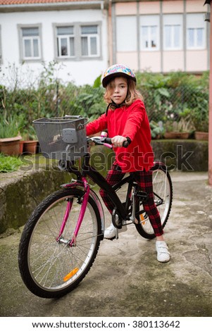 Little girl with her bicycle outdoors. She is looking at camera.