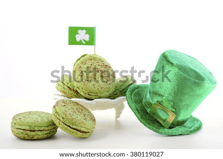 St Patricks Day green macarons with shamrock flags and leprechaun hat on white wood table background. 