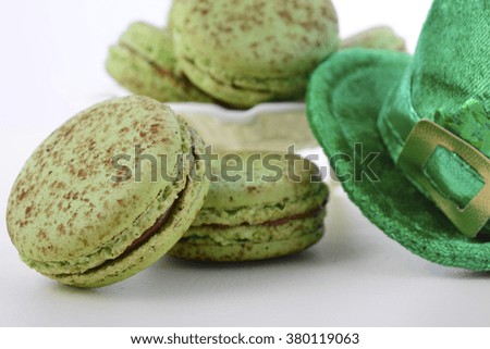 St Patricks Day green macarons with shamrock flags and leprechaun hat on white wood table background, closeup.  