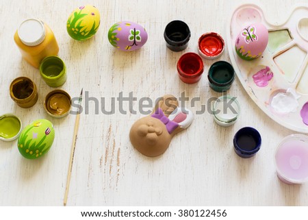 Preparation for Easter: colored eggs, easter bunny, paint, brush, palette. Top view